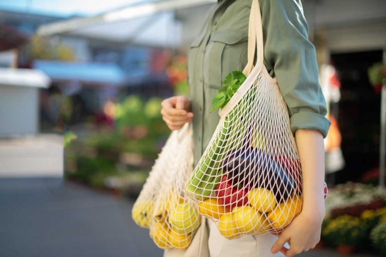 Girl is holding mesh shopping bag and cotton shopper with vegetables without plastic bags at farmers market
