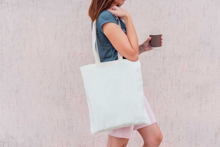 Young woman with white cotton bag and paper coffee cup in her hands