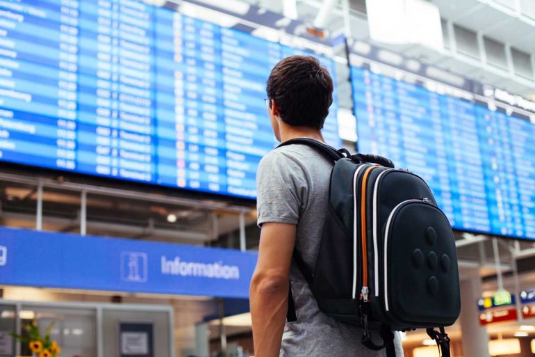 Young man with backpack in airport near flight timetable