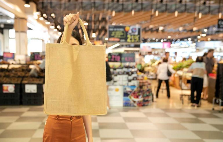 Asian Women carrying fabric bag towards camera in front of grocery stores
