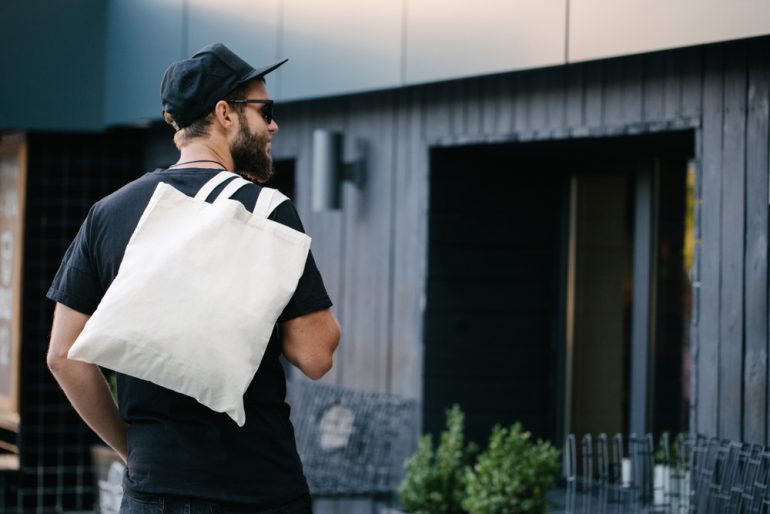 Young man holding white textile eco bag against urban city background