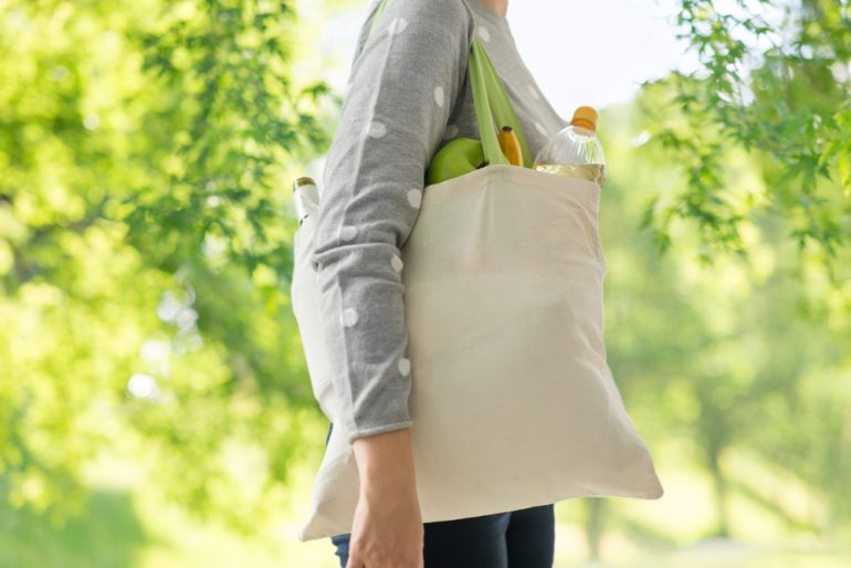 woman with white reusable canvas bag for food shopping over green natural background